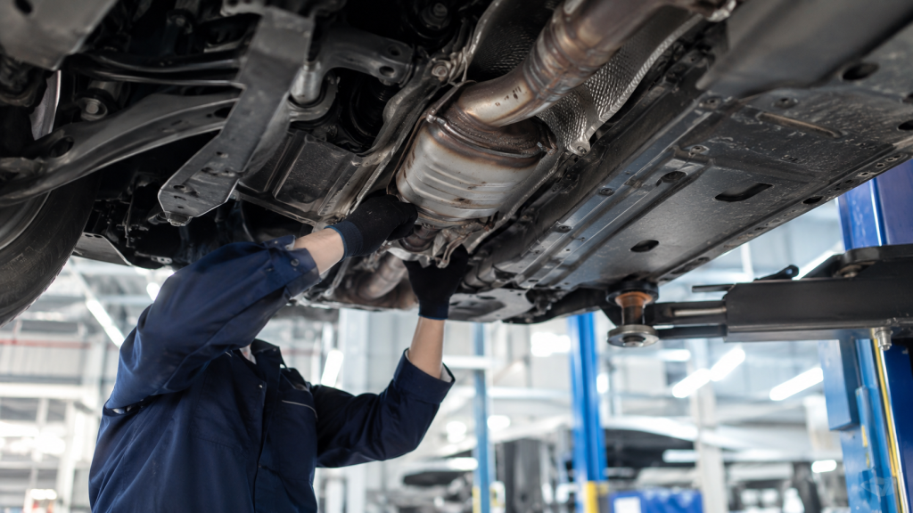 Kỹ thuật viên kiểm tra bộ chuyển đổi xúc tác dưới gầm ô tô trong garage