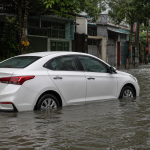 Ô tô sedan trắng đỗ trên đường phố ngập nước sau cơn mưa lớn